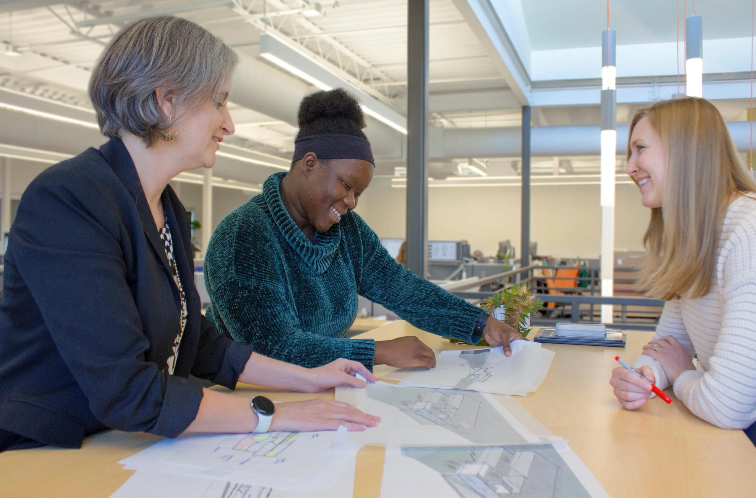 A team of three HH Architecture employees huddled around a table looking at sketches