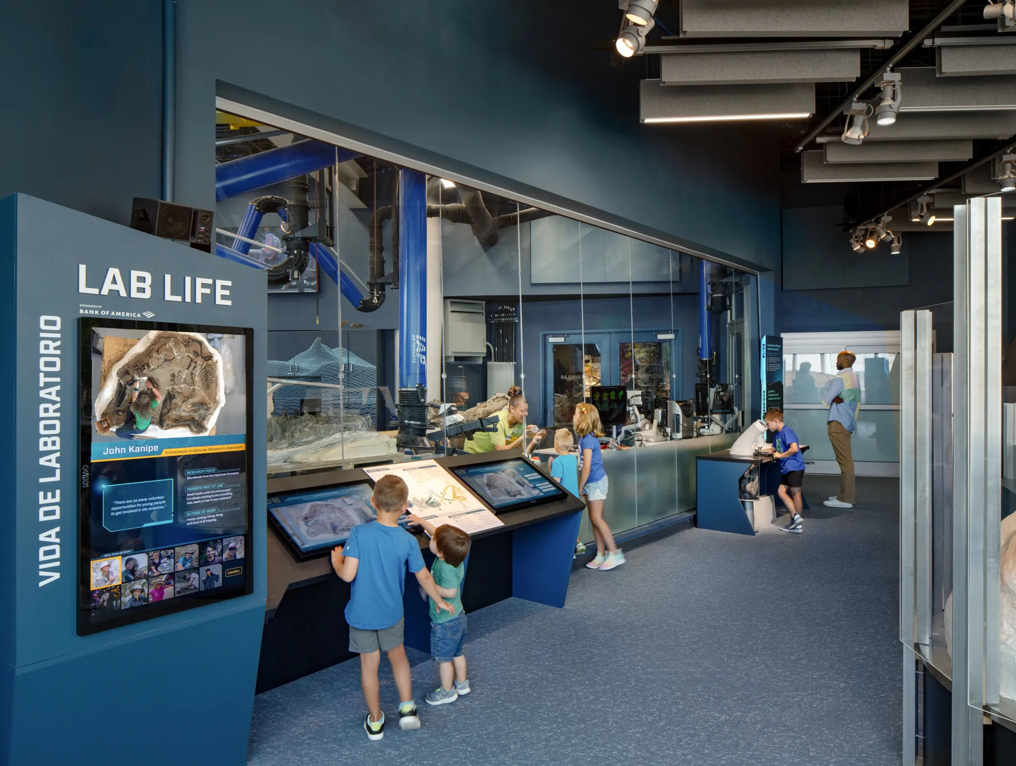 Children and museum guests look into the Dueling Dinosaurs Laboratory Exhibit at the North Carolina Museum of Natural Sciences